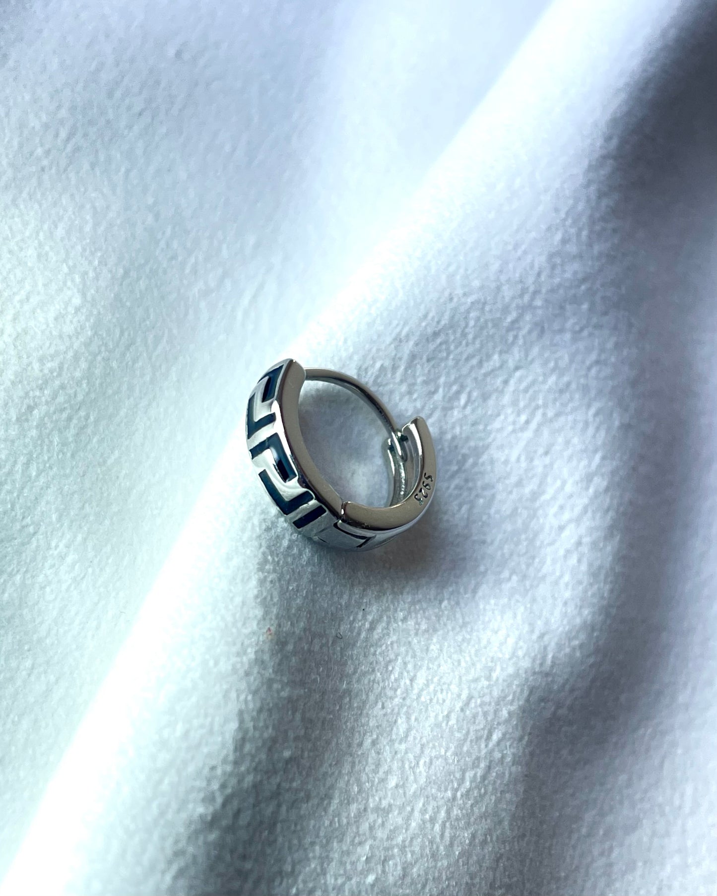 925 Silver hoop earring with geometric design on a white fabric background